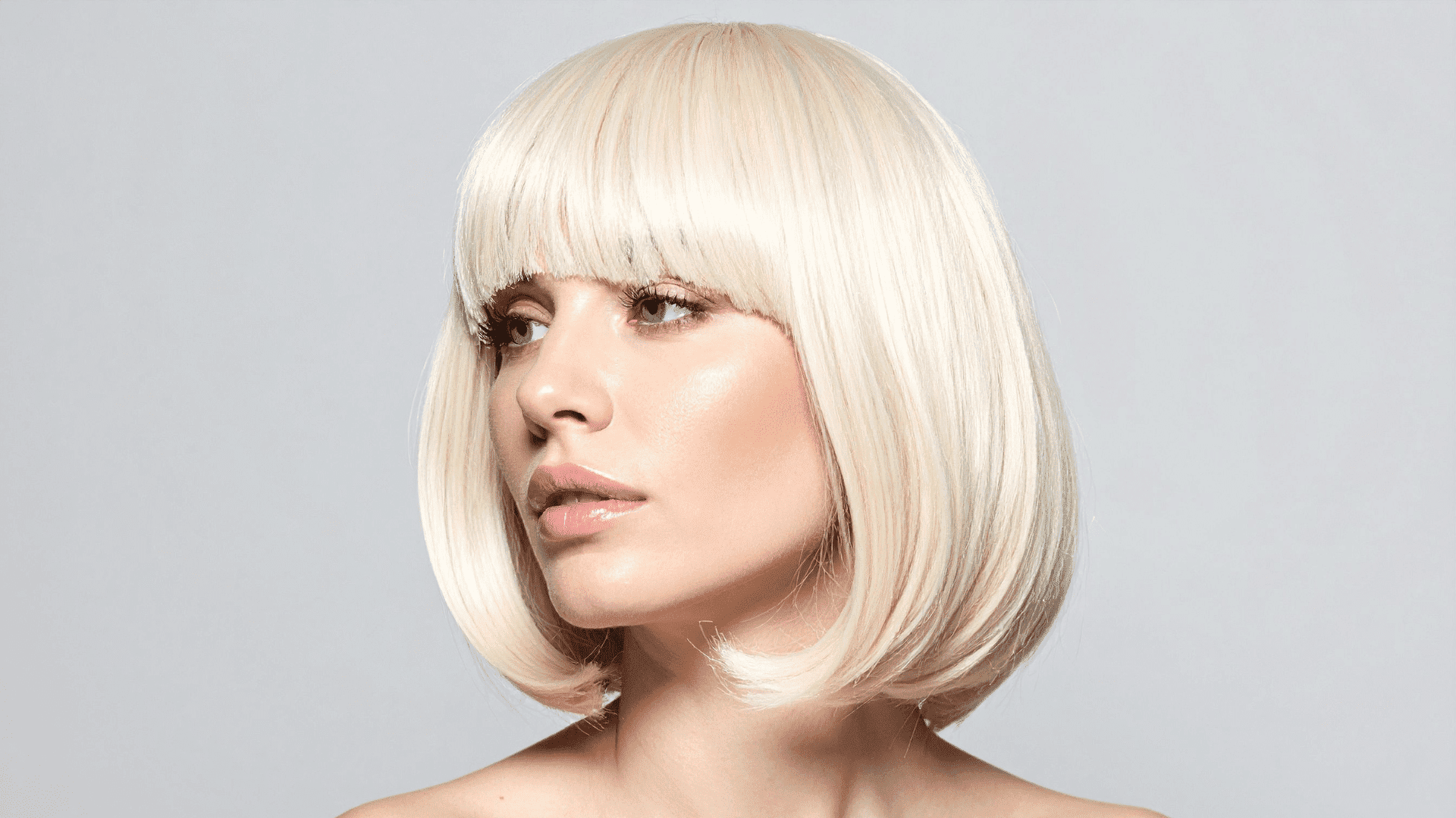 Short-haired person with platinum blonde bob haircut, looking to the side against a gray background.