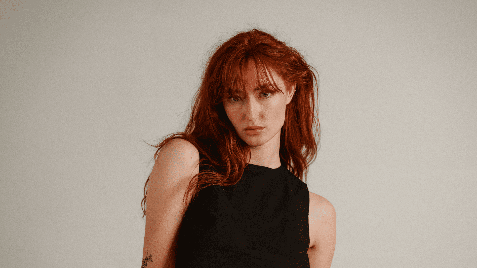 Young woman with red hair in a black top against a neutral background.