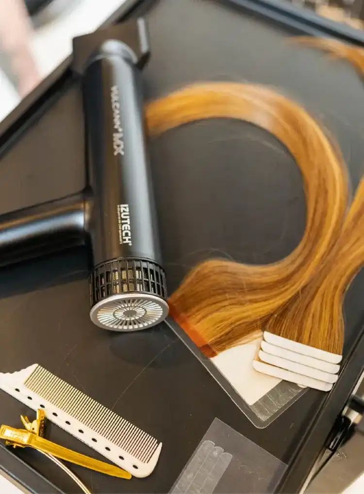 Hair styling tools with a comb, blow dryer, and hair strands on a salon table.