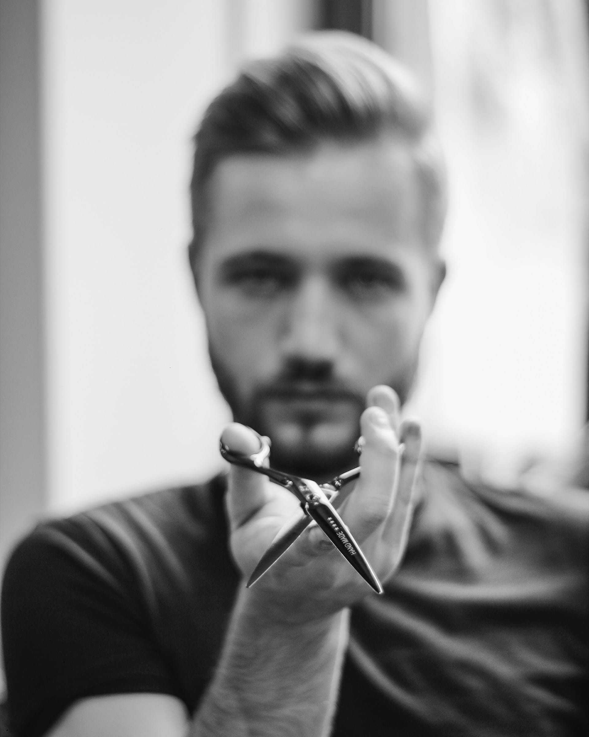A barber holds scissors focused on hand, blurred background.